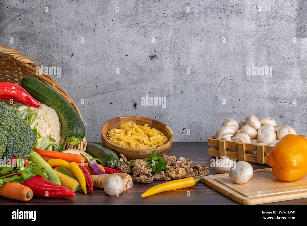 Varie verdure fresche come peperoni, cavolfiore, peperoni, funghi e broccoli intorno e in un cestino con una ciotola di pasta accanto ad essa su una Foto Stock