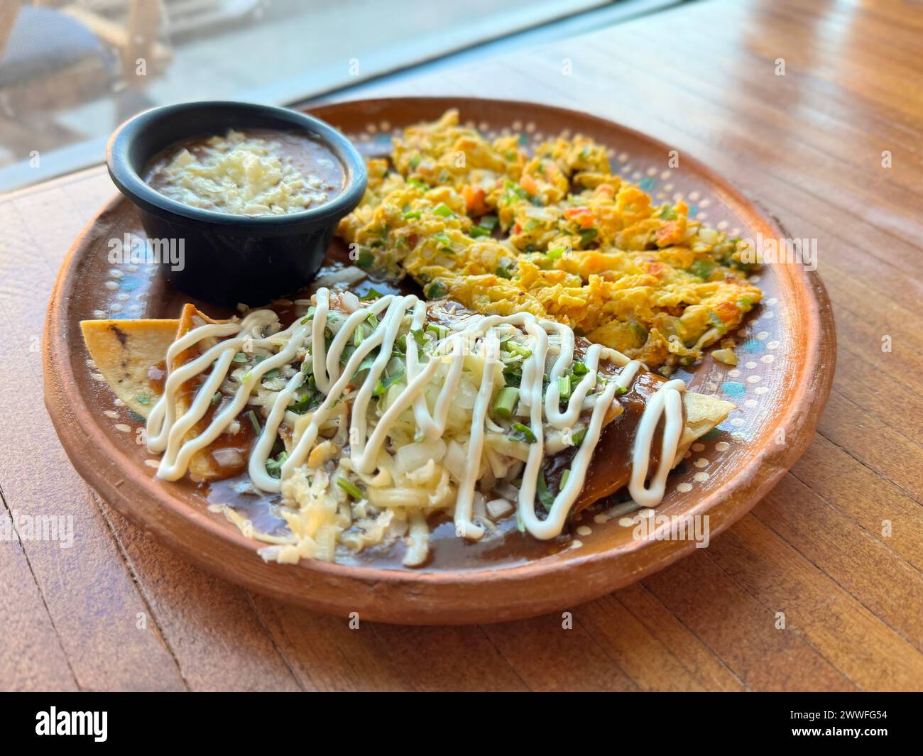 Colazione messicana tradizionale con "huevos a la mexicana", chilaquile con crema e un lato di fagioli conditi con formaggio, serviti su ru Foto Stock