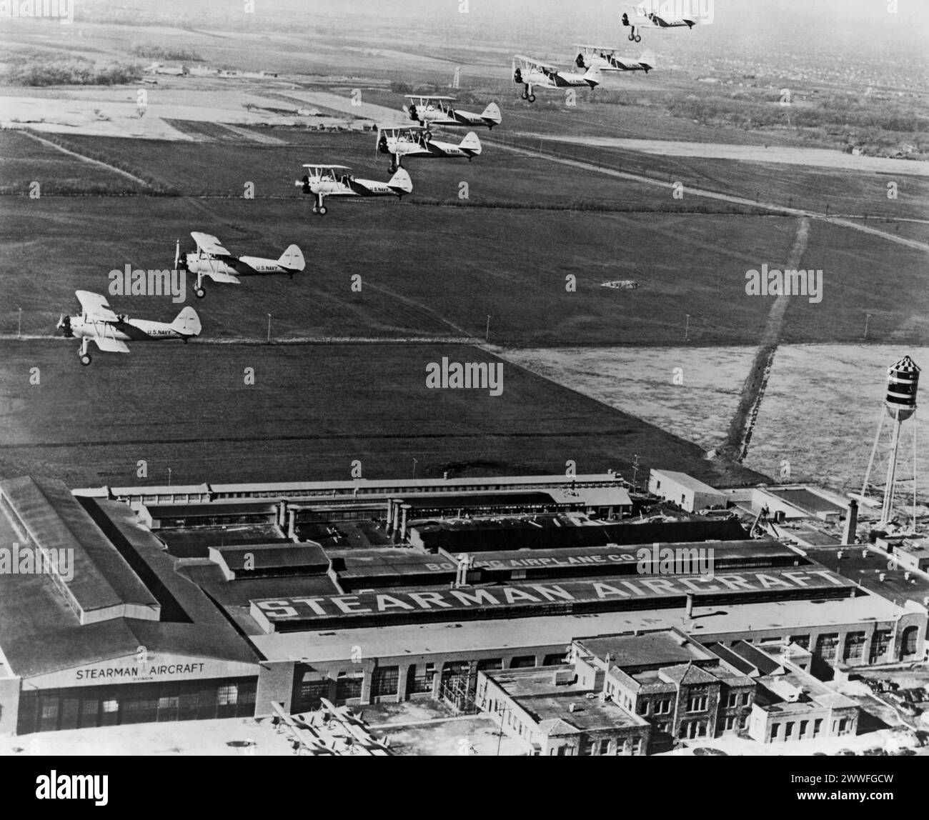 Wichita, Kansas, 1934 Una scena tipica a Wichita, Kansas, quasi ogni giorno è vedere un gruppo di aerei da addestramento di base come questi che fanno il loro volo di partenza dallo stabilimento di Stearman. Gli otto aerei di questa formazione sono nuovi N2S-1 della Marina appena usciti dalla linea di produzione, lasciando la fabbrica sulla strada per svolgere il loro ruolo nel programma di addestramento della difesa Nazionale. La Stearman Aircraft Division della Boeing Airplane Co sta effettuando consegne di quantità regolari su ordini della US Navy e dell'US Army Air Corps per un aumento di 3000 addestratori primari, il più grande numero mai ordinato dall'U Foto Stock