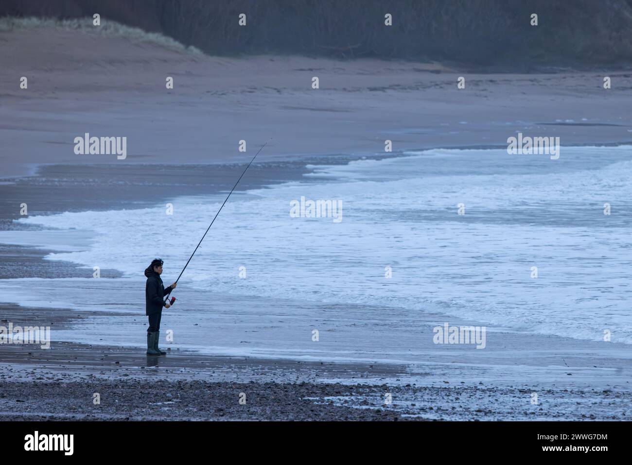 Uomo che pesca da Freshwater East Beach nel Pembrokeshire, Galles Foto Stock