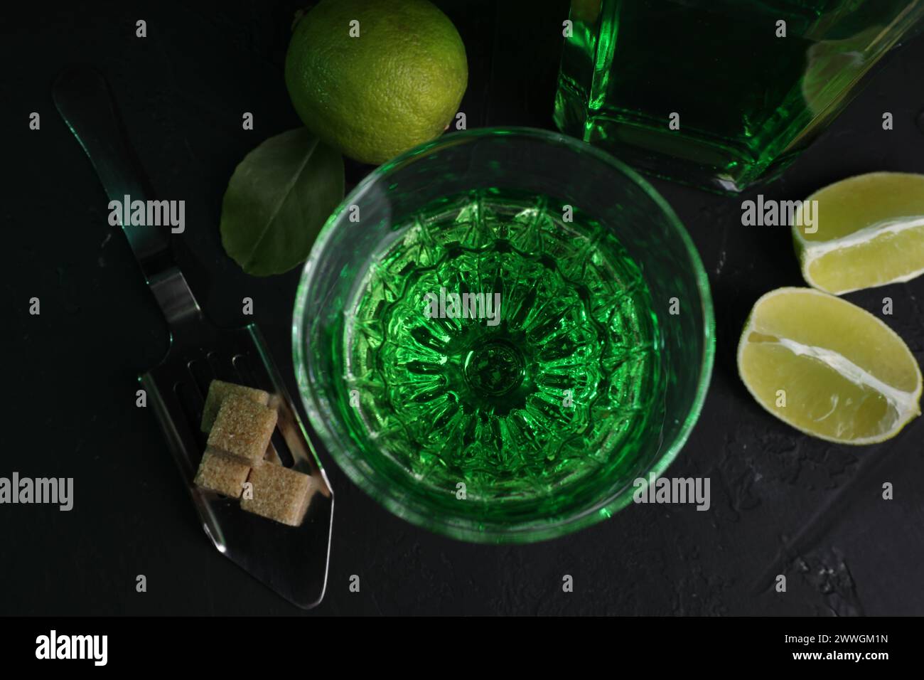 Absinthe in vetro, cucchiaio, zucchero di canna e lime su un tavolo nero, stendere in piano. Bevanda alcolica Foto Stock