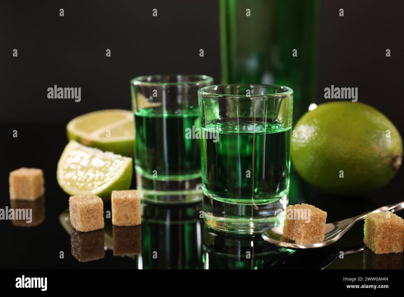 Absinthe in bicchieri da shot, zucchero di canna, lime e cucchiaio sul tavolo a specchio. Bevanda alcolica Foto Stock