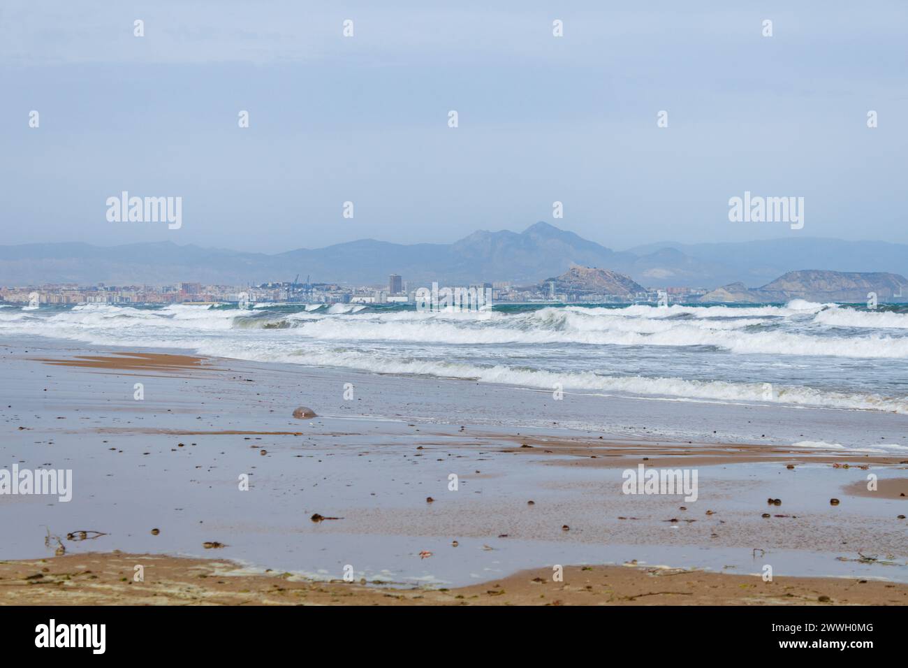 Forte giornata ventosa sulla baia di Alicante con la città sullo sfondo e forti onde dalla spiaggia di El Altet, Spagna Foto Stock