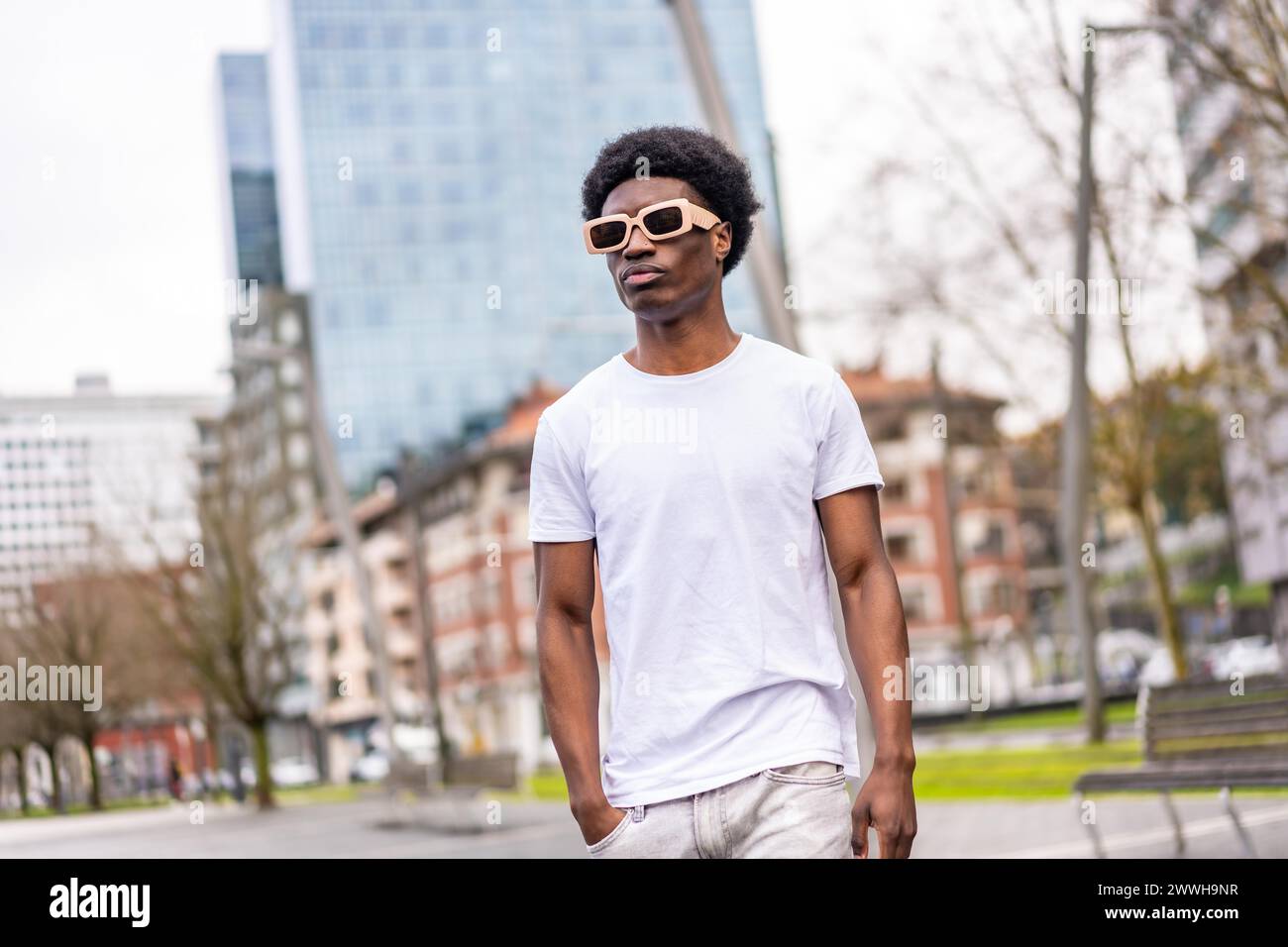 Giovane e fresco uomo africano con abiti bianchi e occhiali da sole che camminano lungo la città Foto Stock