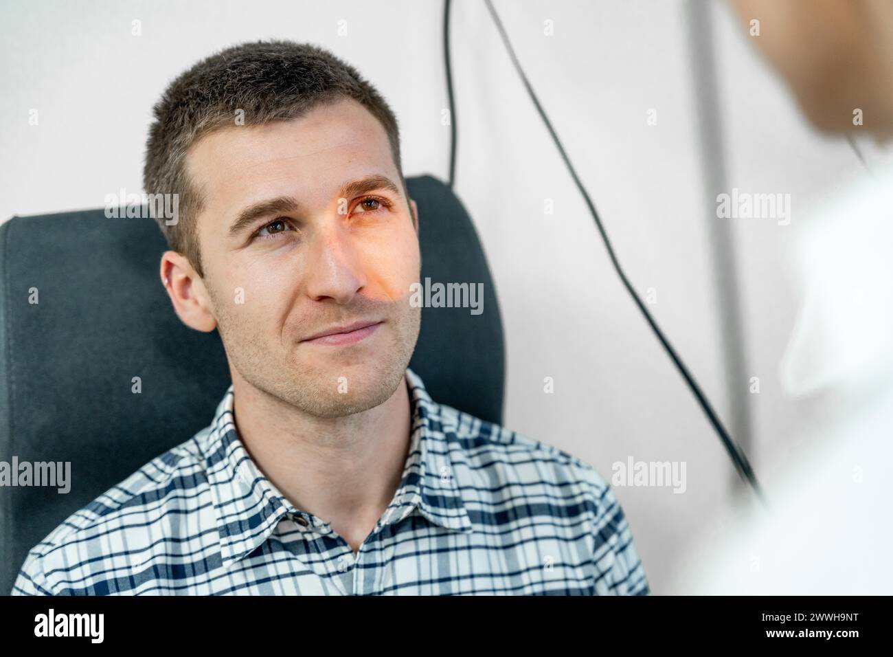 Oftalmologo donna che illumina l'occhio di un uomo per controllare la retina con un retinoscopio Foto Stock
