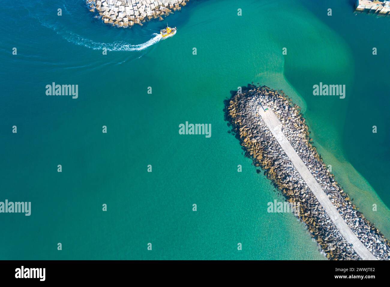 una barca da pesca che entra in un porto protetto da una frangiflutti, acque turchesi. Fotografia con i droni Foto Stock