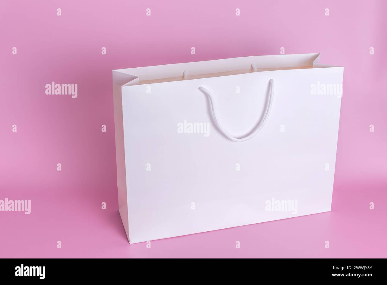 Un grande sacchetto di carta bianca con manici di corda bianchi si staglia su uno sfondo rosa in primo piano. Foto Stock