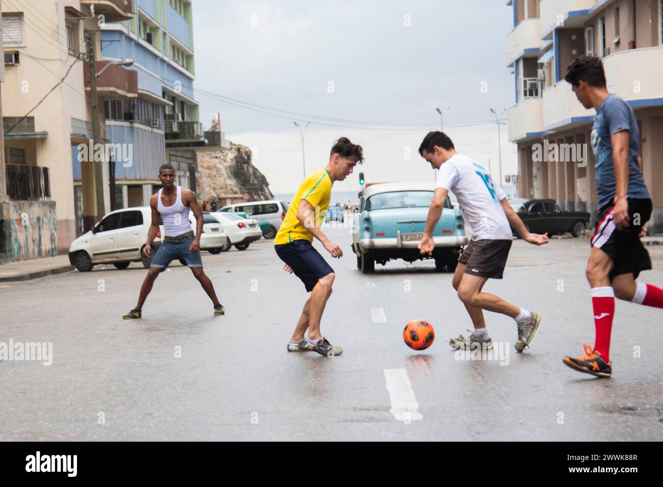 I giovani cubani calciano una palla di calcio giocando una partita in mezzo alla strada a l'Avana, Cuba. Foto Stock