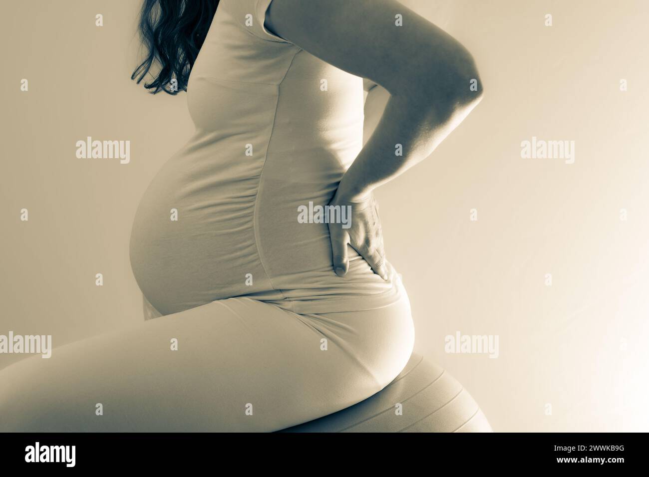 Descrizione: La donna incinta con bambole tratta il mal di schiena e con l'aiuto di una palla da palestra. Ultimo mese di gravidanza - settimana 36. Vista laterale. Schiena bianca Foto Stock