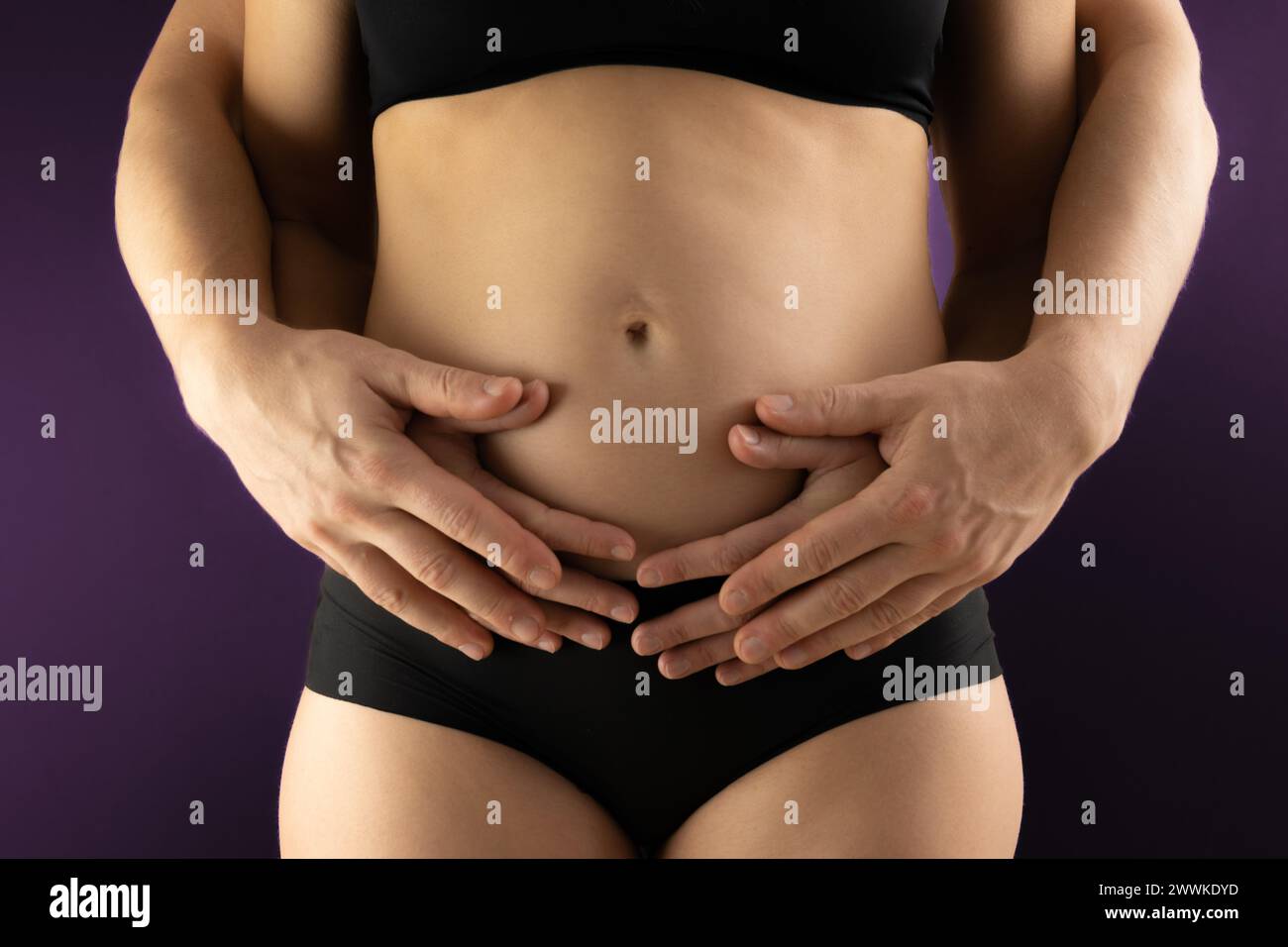 Descrizione: Vista della sezione centrale di genitori irriconoscibili che tengono le mani delicatamente sulla pancia incinta nei primi mesi di gravidanza. Prima la gravidanza Foto Stock