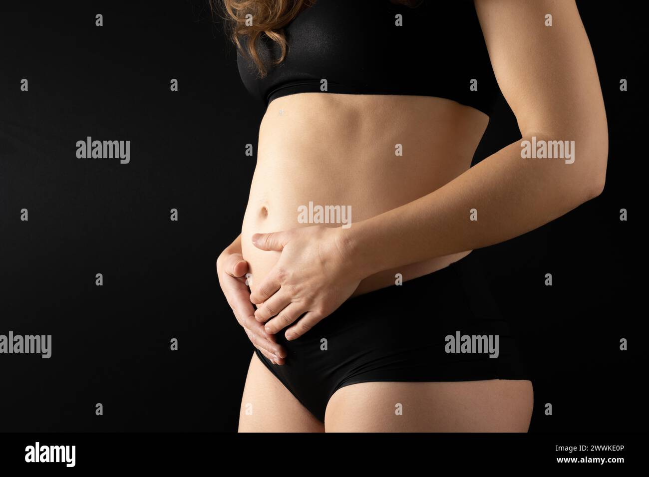 Descrizione: Vista in sezione intermedia di una donna irriconoscibile che tiene dolcemente la pancia nei primi mesi di gravidanza. Gravidanza primo trimestre - settimana 18. Lato Foto Stock