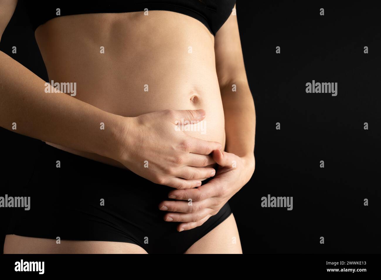 Descrizione: Vista in sezione intermedia di una donna irriconoscibile che tiene delicatamente la pancia durante i primi mesi di gravidanza. Gravidanza primo trimestre - settimana 18. S Foto Stock