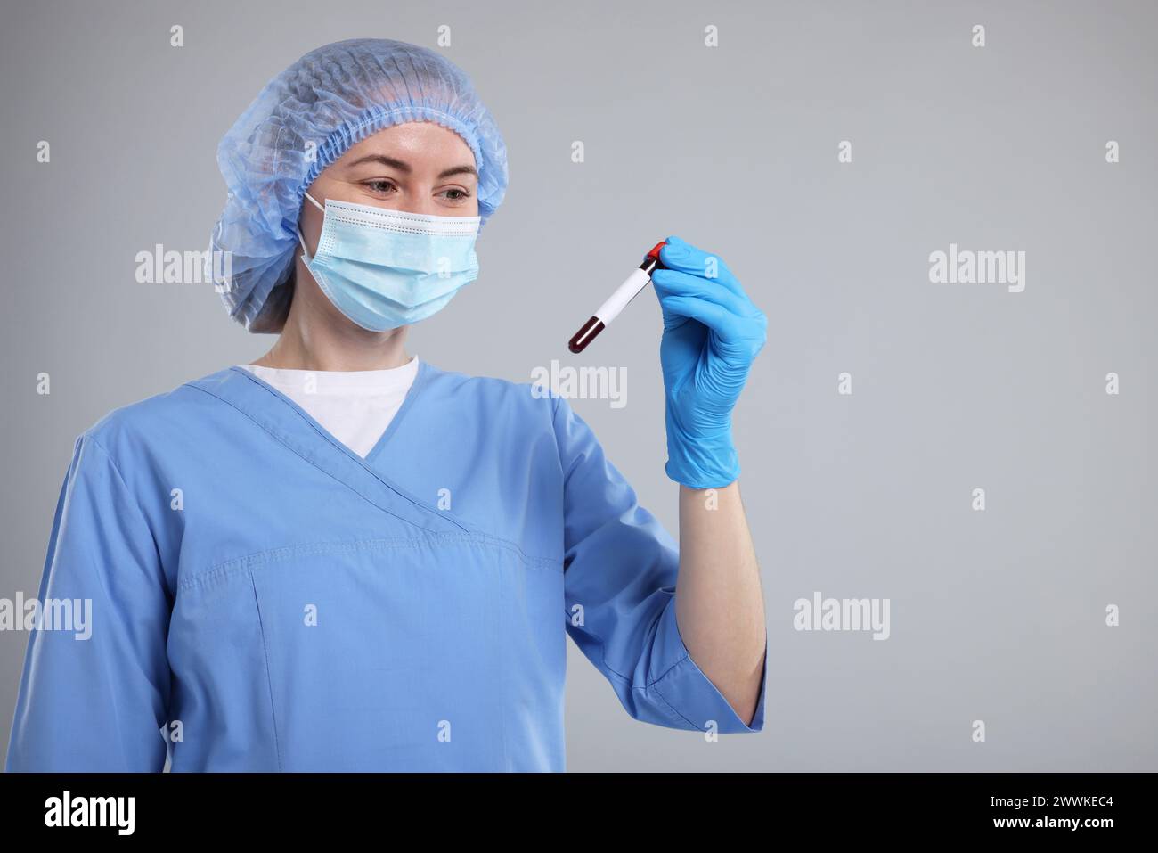 Analisi di laboratorio. Medico con campione di sangue nella provetta su sfondo grigio chiaro, spazio per testo Foto Stock