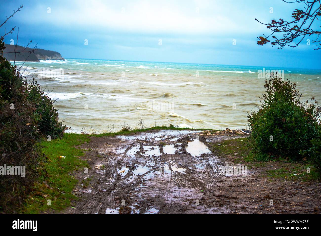 Esplora l'aspra bellezza di un terreno fangoso sulla costa, impresso con tracce di pneumatici, che mostrano l'interazione dinamica tra natura e attività umana. Foto Stock