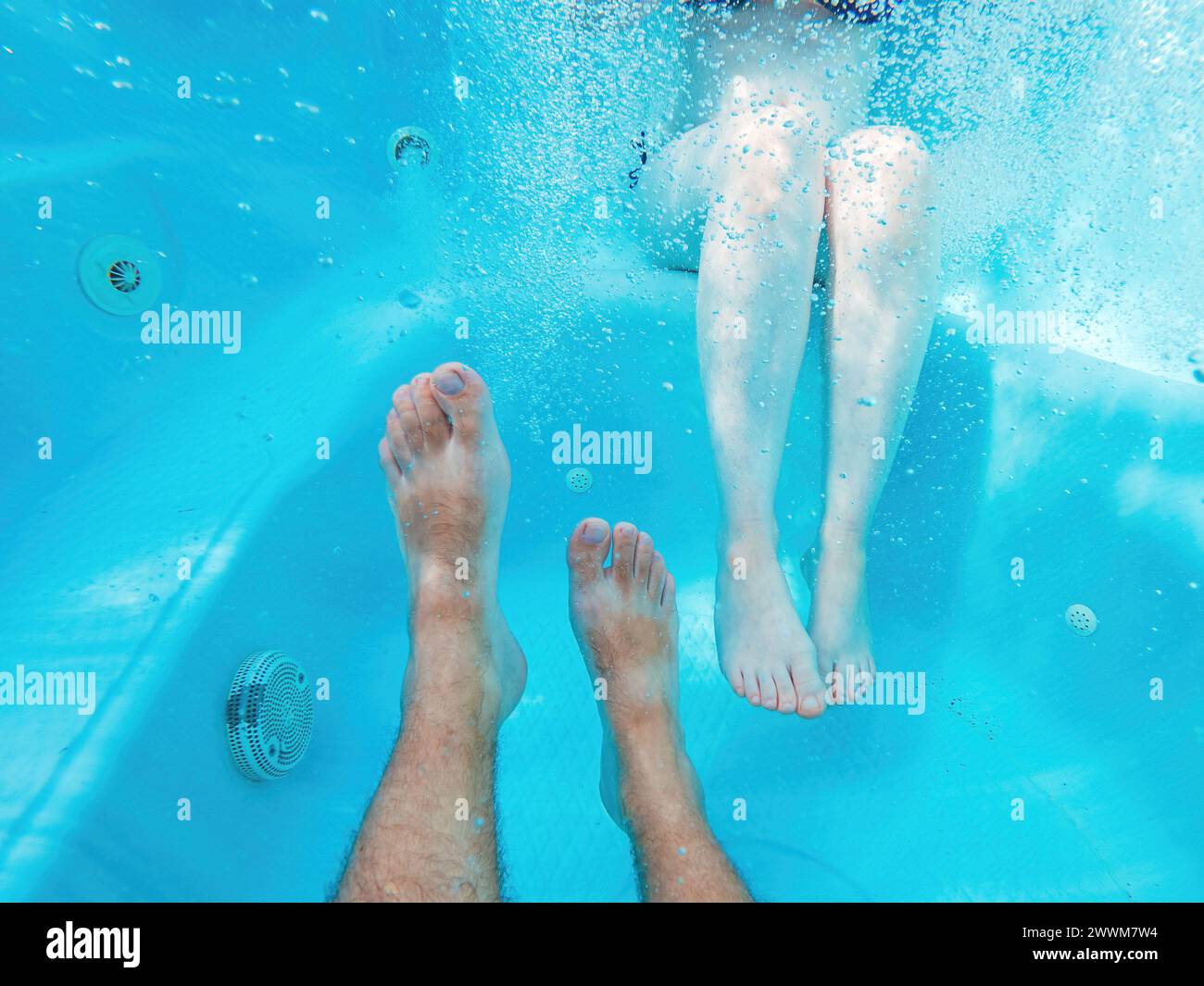 Coppia nella vasca idromassaggio, ripresa subacquea di gambe maschili e femminili in acqua, messa a fuoco selettiva Foto Stock