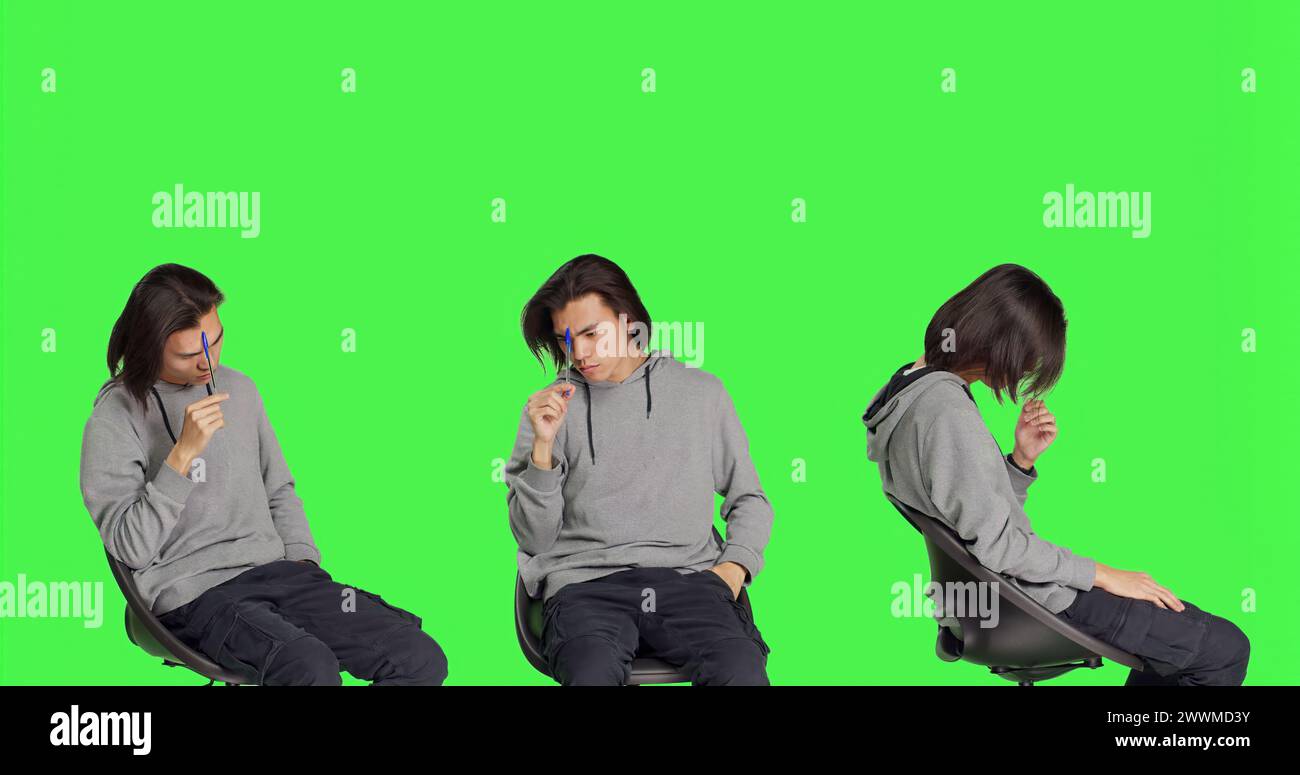 Modello maschile che pensa alla soluzione sullo sfondo verde, sentendosi incerto sul nuovo dilemma. Uomo asiatico seduto su una sedia e che agisce confuso, penoso e premuroso. Foto Stock