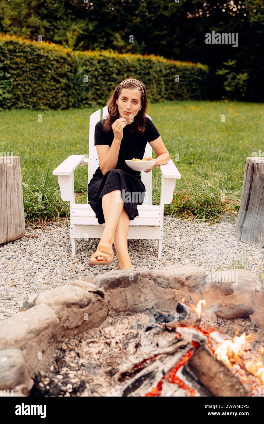 Una donna seduta vicino a un incendio in un campo erboso Foto Stock