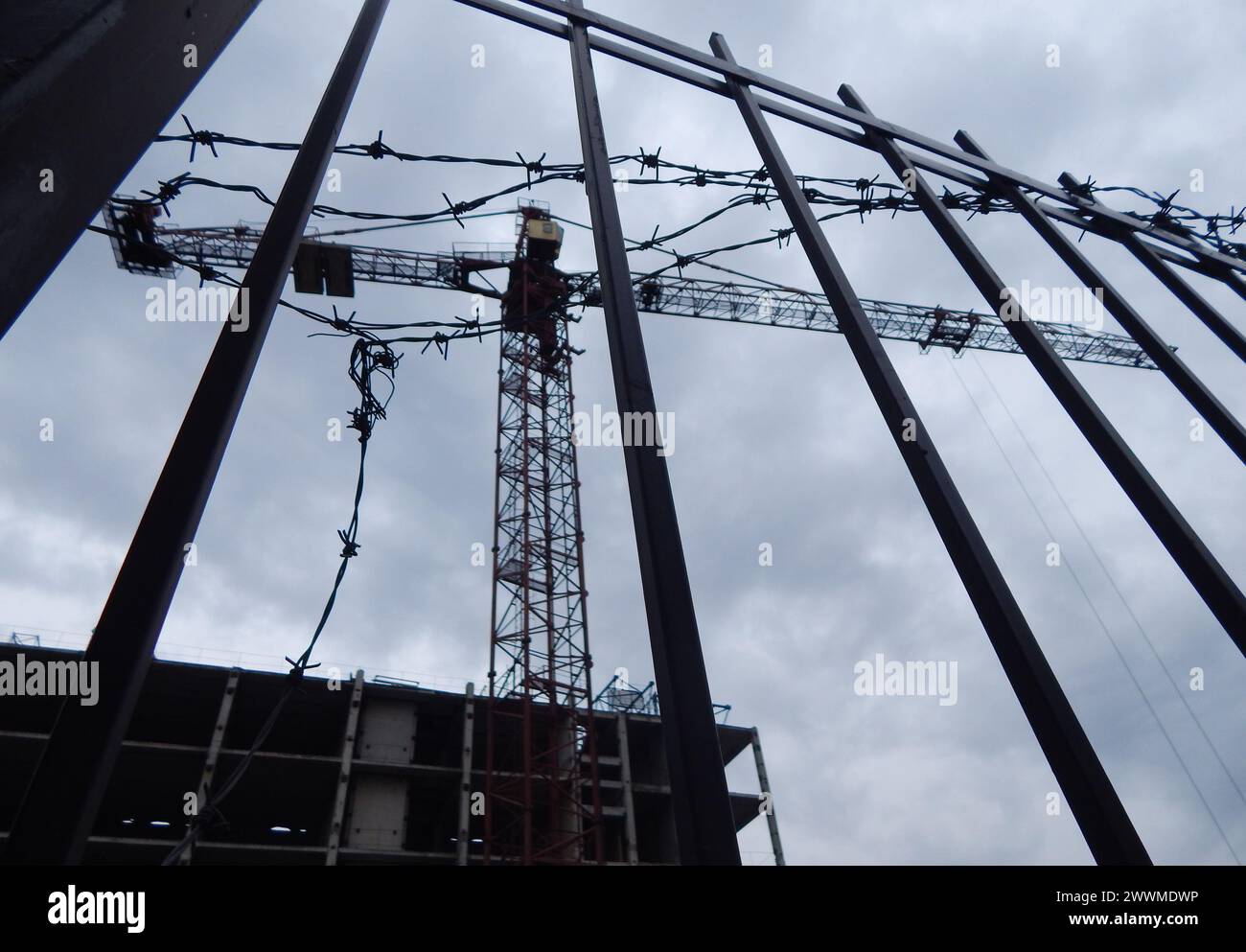 Cantiere non finito recintato con filo spinato e una gru da costruzione sfocata sullo sfondo Foto Stock