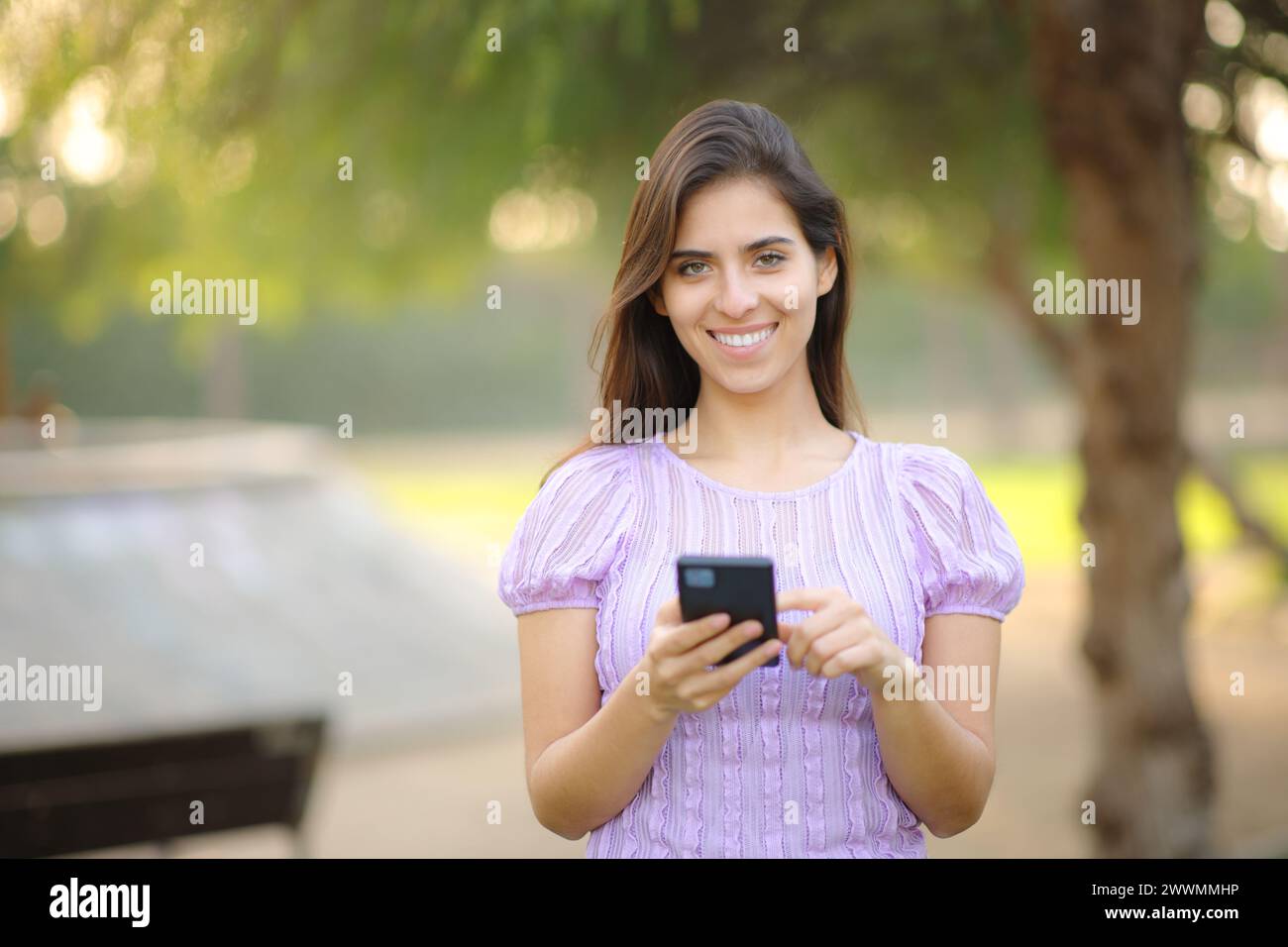 Vista frontale ritratto di una donna felice che tiene il telefono in un parco Foto Stock
