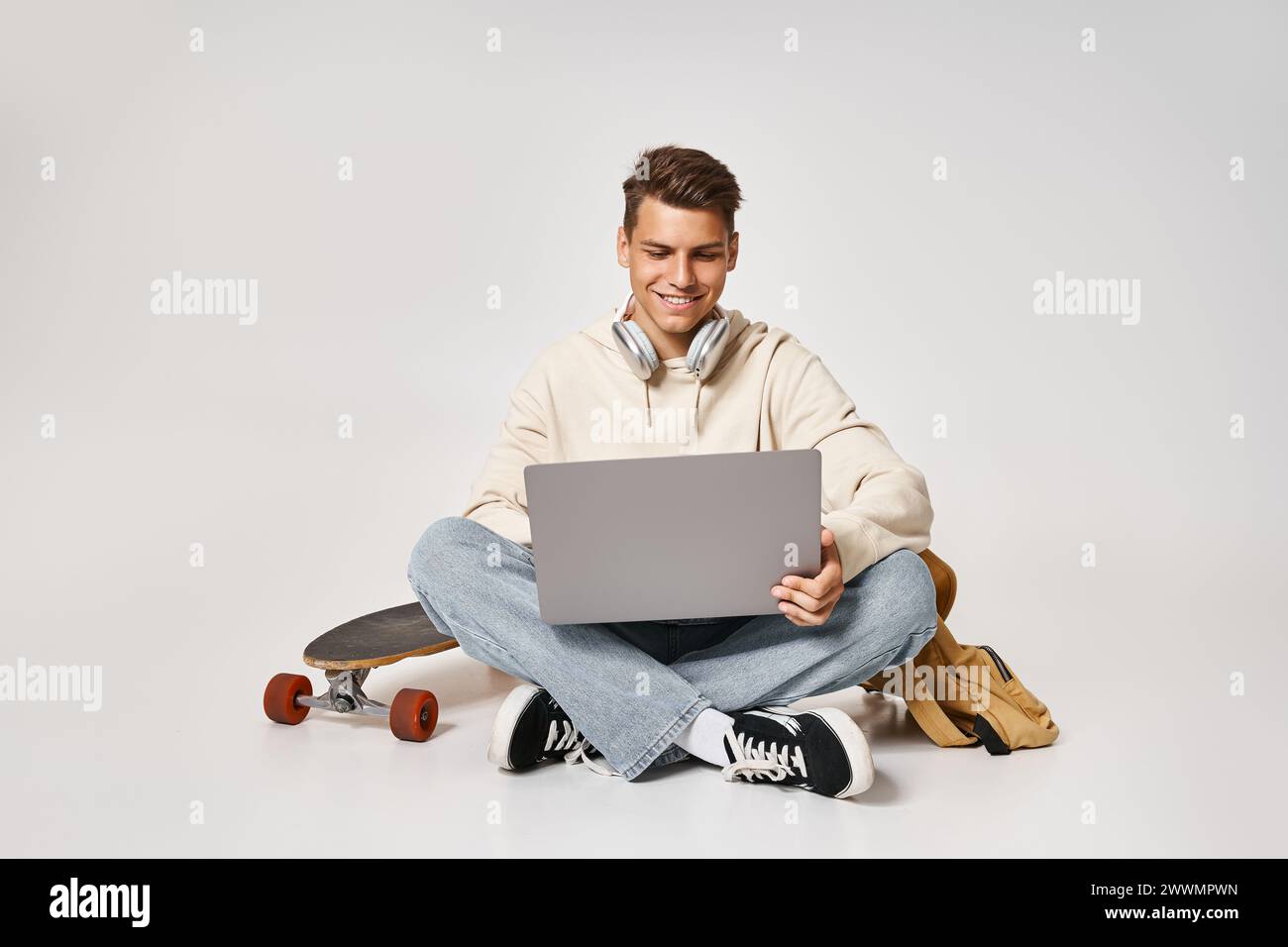 studente intelligente in cuffie che collega il computer portatile e si siede con zaino e skateboard Foto Stock