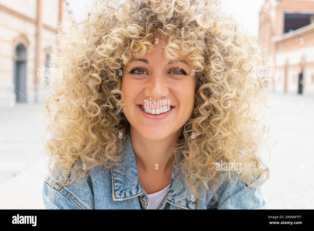 Ritratto di una giovane donna caucasica sorridente con capelli biondi ricci Foto Stock