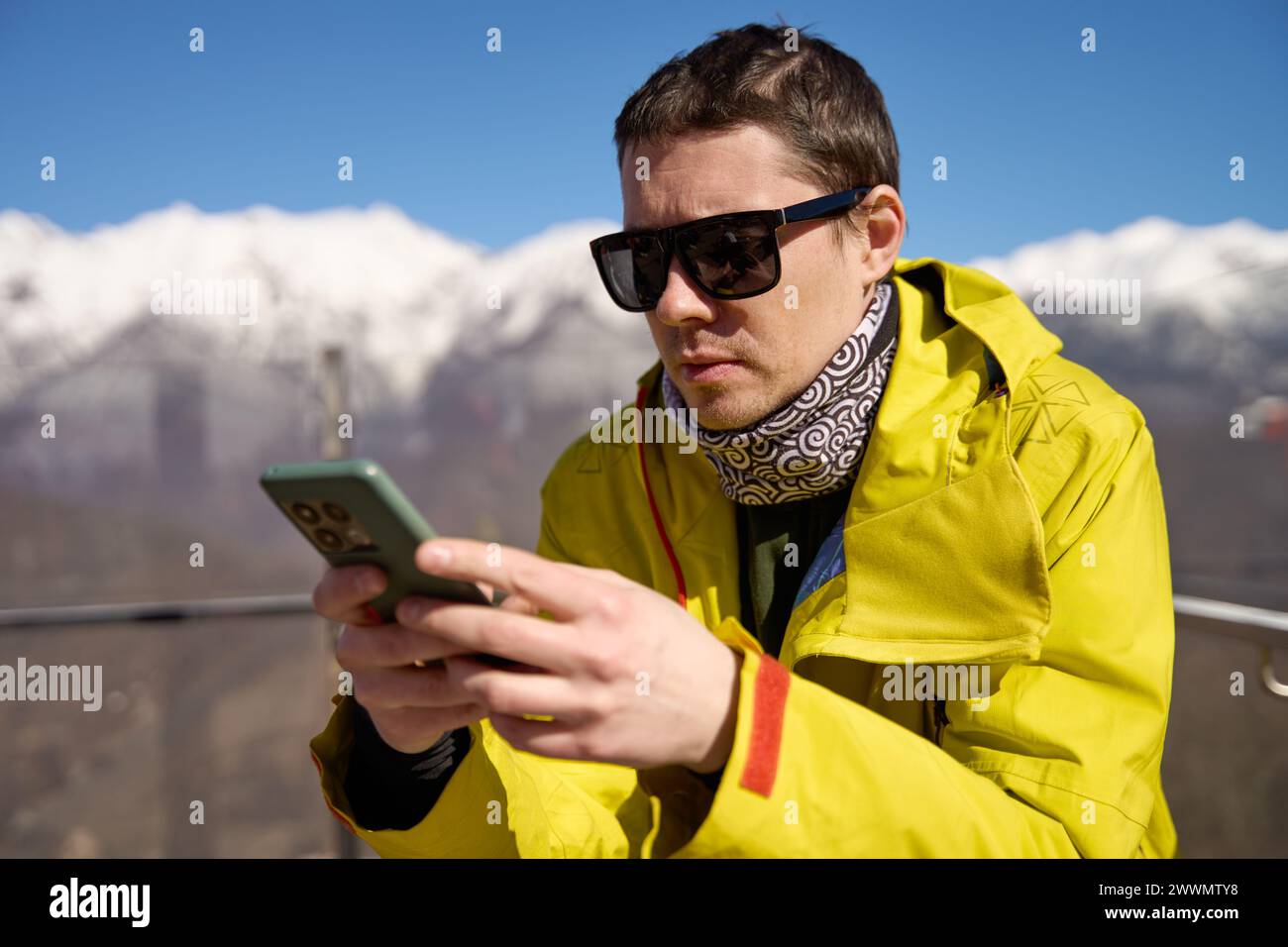 Uomo con attrezzatura da sci che utilizza uno smartphone con montagne innevate sullo sfondo. Foto Stock