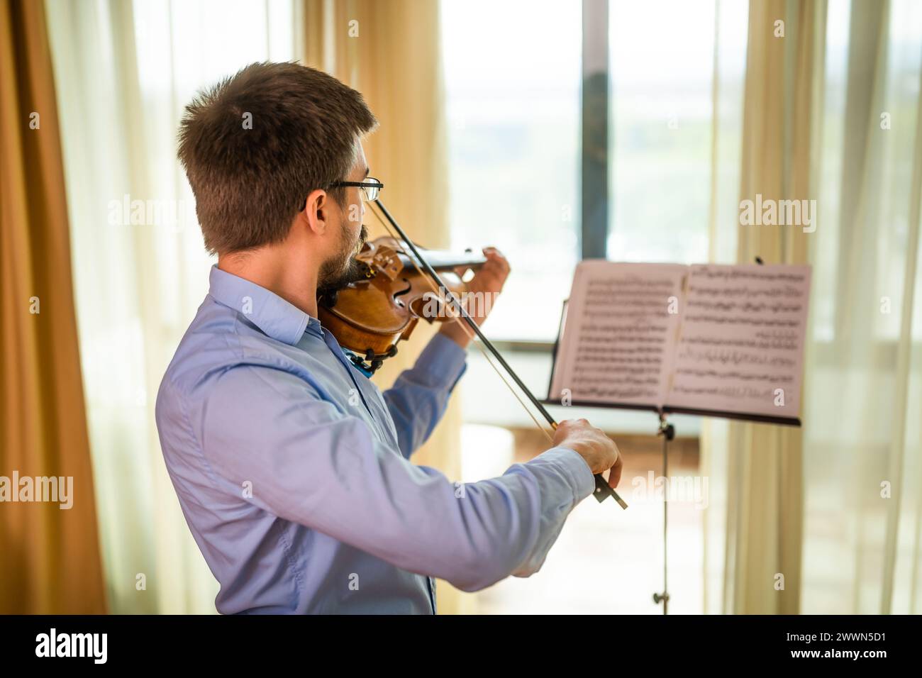 Uomo che suona il violino a casa. Si sta esercitando per le esibizioni dal vivo. Foto Stock
