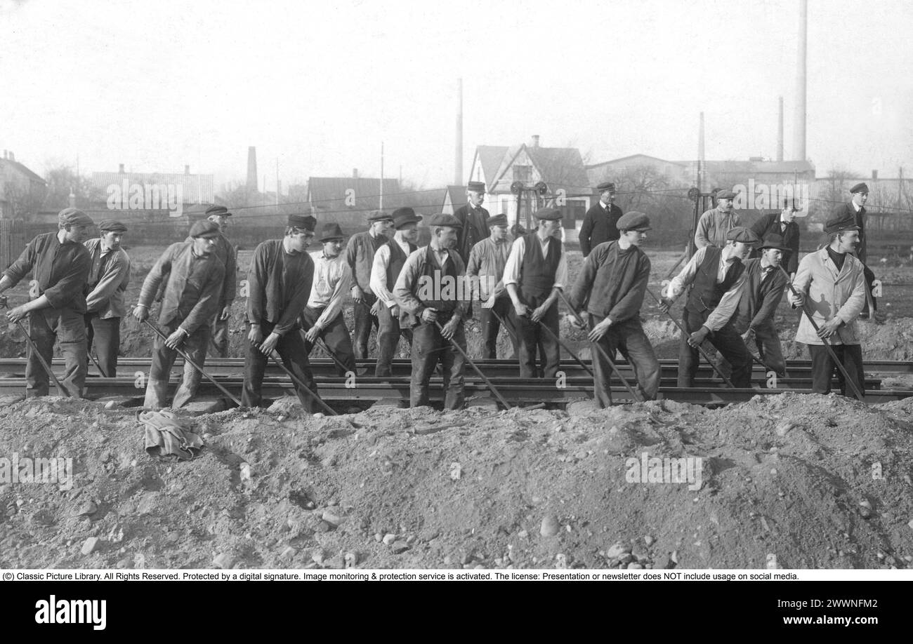 Costruzione di ferrovie. Il gruppo di lavoratori della costruzione ferroviaria tra di loro è visto in uno sforzo di squadra con barre di scavo, che spostano la ferrovia in posizione. anni '1900 Foto Stock