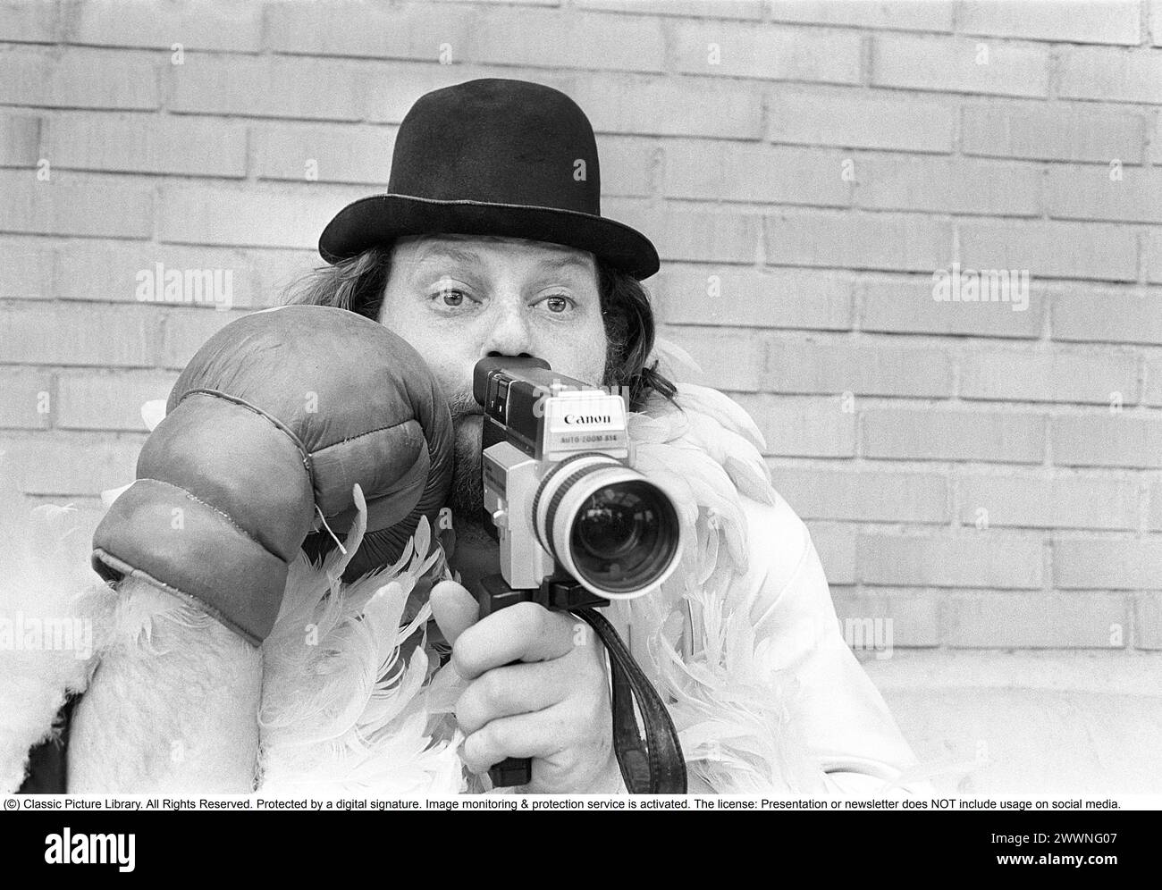 Negli anni '1970 Un uomo sta filmando con una macchina fotografica amatoriale. Il film è stato poi sviluppato e mostrato su un proiettore cinematografico su uno schermo pieghevole a casa. Ricky Bruch (1946-2011) atleta svedese di atletica leggera. Era noto per essere un po' uno showman qui raffigurato con guanti da boxe, una boa di piume e un cappello. 1975 Foto Stock