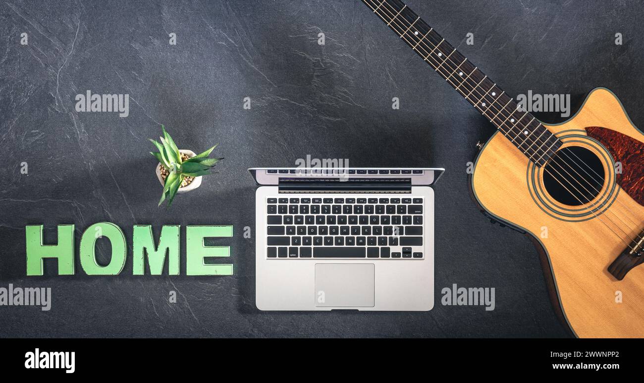 Chitarra acustica, laptop e parola decorativa Home su sfondo scuro, vista dall'alto. Foto Stock