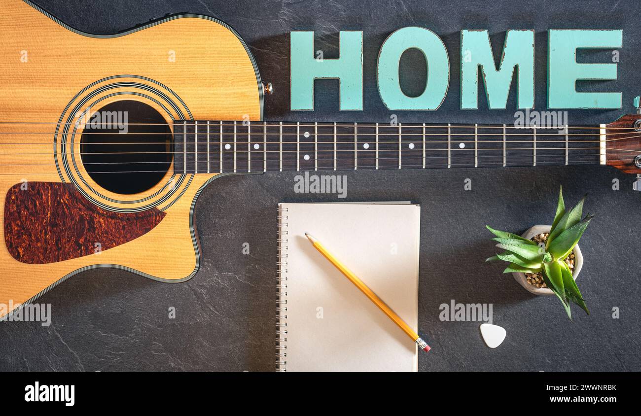 Chitarra acustica, blocco note e parola decorativa Home, vista dall'alto. Foto Stock