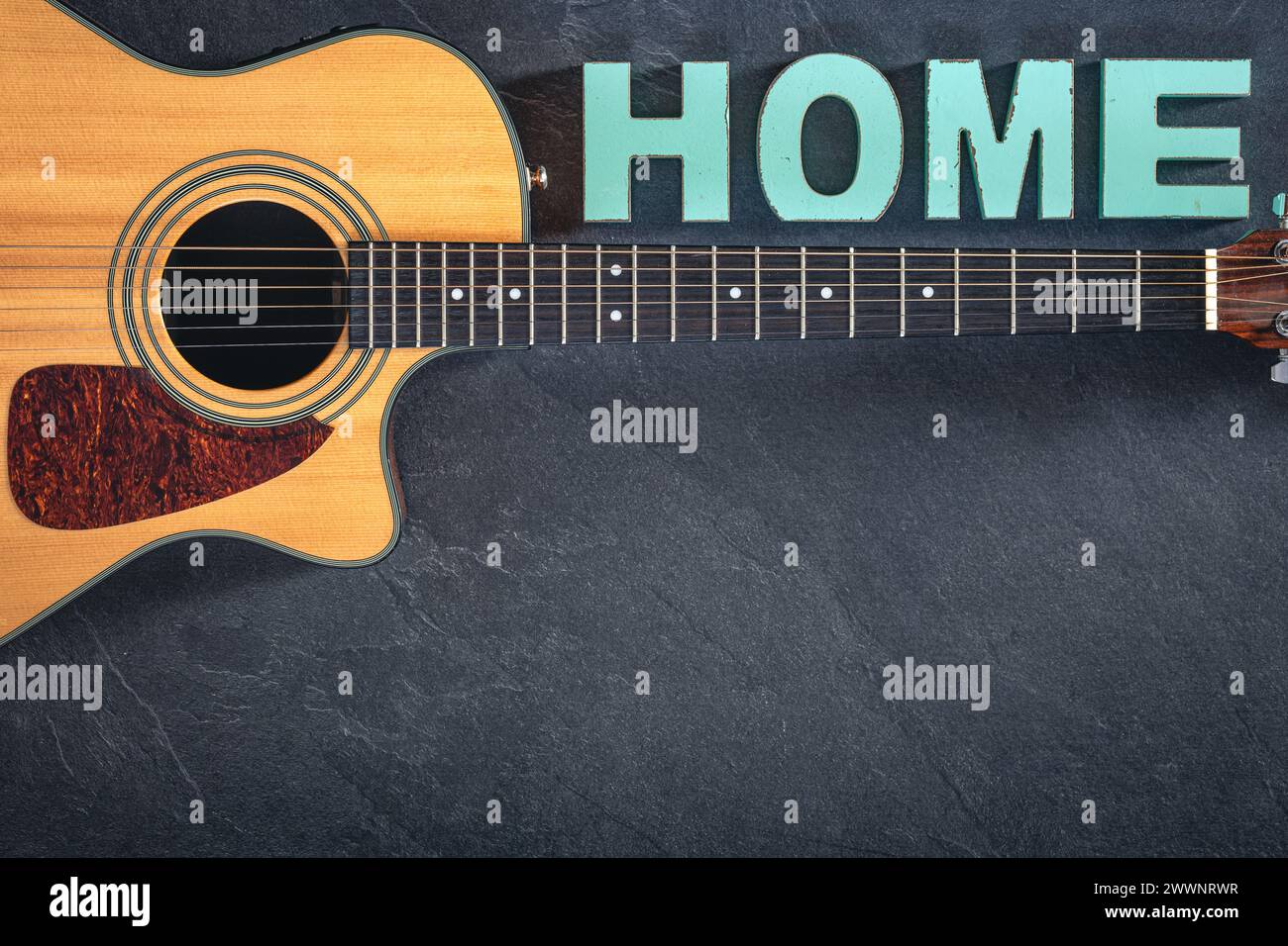 Chitarra acustica e parola decorativa Home su sfondo nero testurizzato. Foto Stock