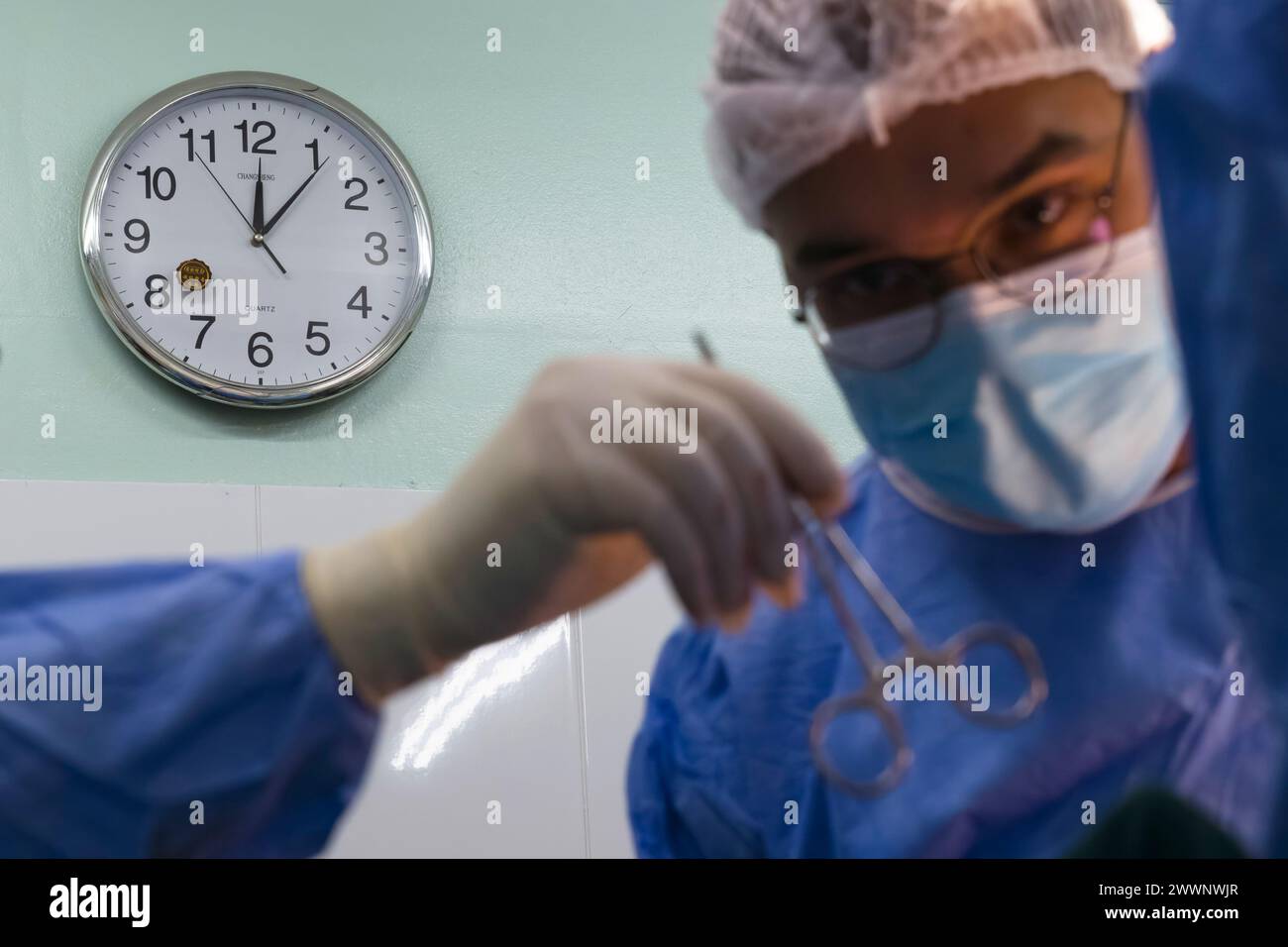 Un orologio analogico è appeso alla parete mentre uno strumento chirurgico viene passato a un medico durante un'operazione al Paramaribo's Academic Hospital in Suriname, 21 febbraio 2024. Quarantadue avieri di servizio attivo e di riserva dell'aeronautica statunitense si sono recati in Suriname a sostegno della missione di assistenza medica delle piccole Antille di quest'anno, prestando servizio negli impegni sanitari, scambiando le migliori pratiche e sviluppando relazioni più forti con i partner della nazione ospitante in medicina. Aeronautica militare Foto Stock