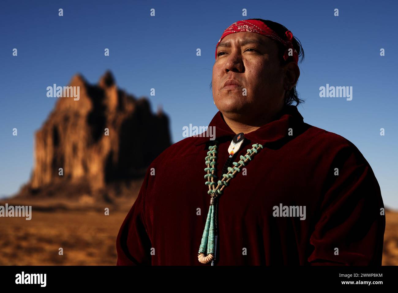 Il sergente tecnico Darrell Charlee, Kirtland Air Force base Inspection Agency client Systems NCO in carica, posa per una foto indossando un tradizionale abbigliamento Navajo di fronte a Shiprock Peak nella riserva Navajo Nation Reservation fuori Shiprock, New Mexico, 28 febbraio 2024. Charlee fornisce competenze di networking per le comunicazioni per garantire la protezione e il funzionamento di hardware e software critici. Dall'installazione dei programmi necessari alla risoluzione dei problemi e alla riparazione di eventuali problemi, questi esperti svolgono un ruolo fondamentale nel mantenere l'accesso e il controllo della tecnologia e delle reti necessarie per la comunicazione Foto Stock