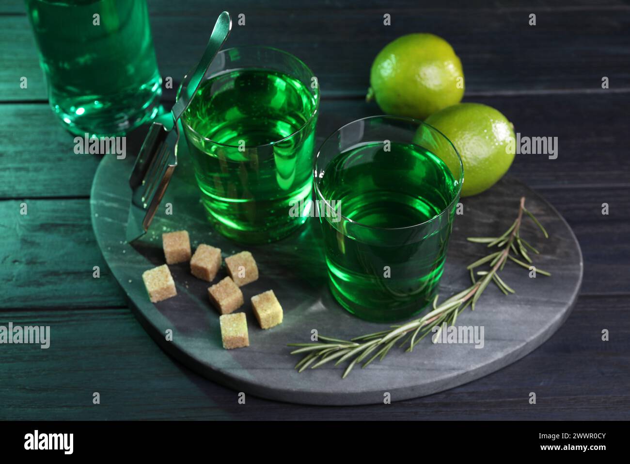 Assenzio in bicchieri, rosmarino, zucchero di canna e calce su un tavolo di legno. Bevanda alcolica Foto Stock