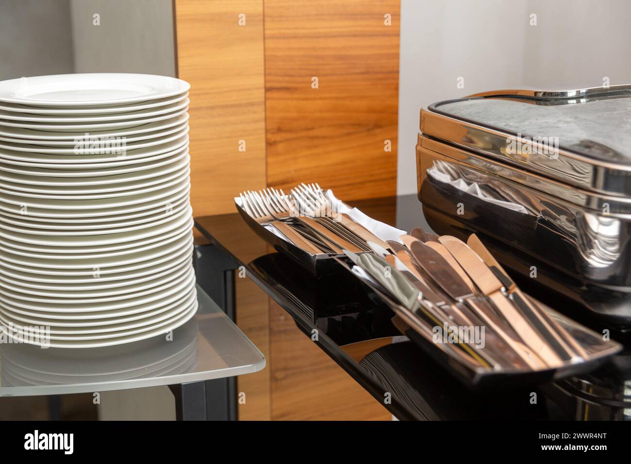 Pila di piatti accanto a piatti a base di chafing chiusi nella sala banchetti per feste. Marmites pronti per il servizio in acciaio inox a buffet. Foto Stock