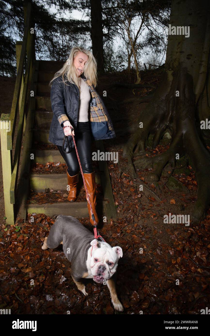 Signora in abito da campagna che cammina il suo bulldog nella sua tenuta di campagna mentre scende i gradini Foto Stock