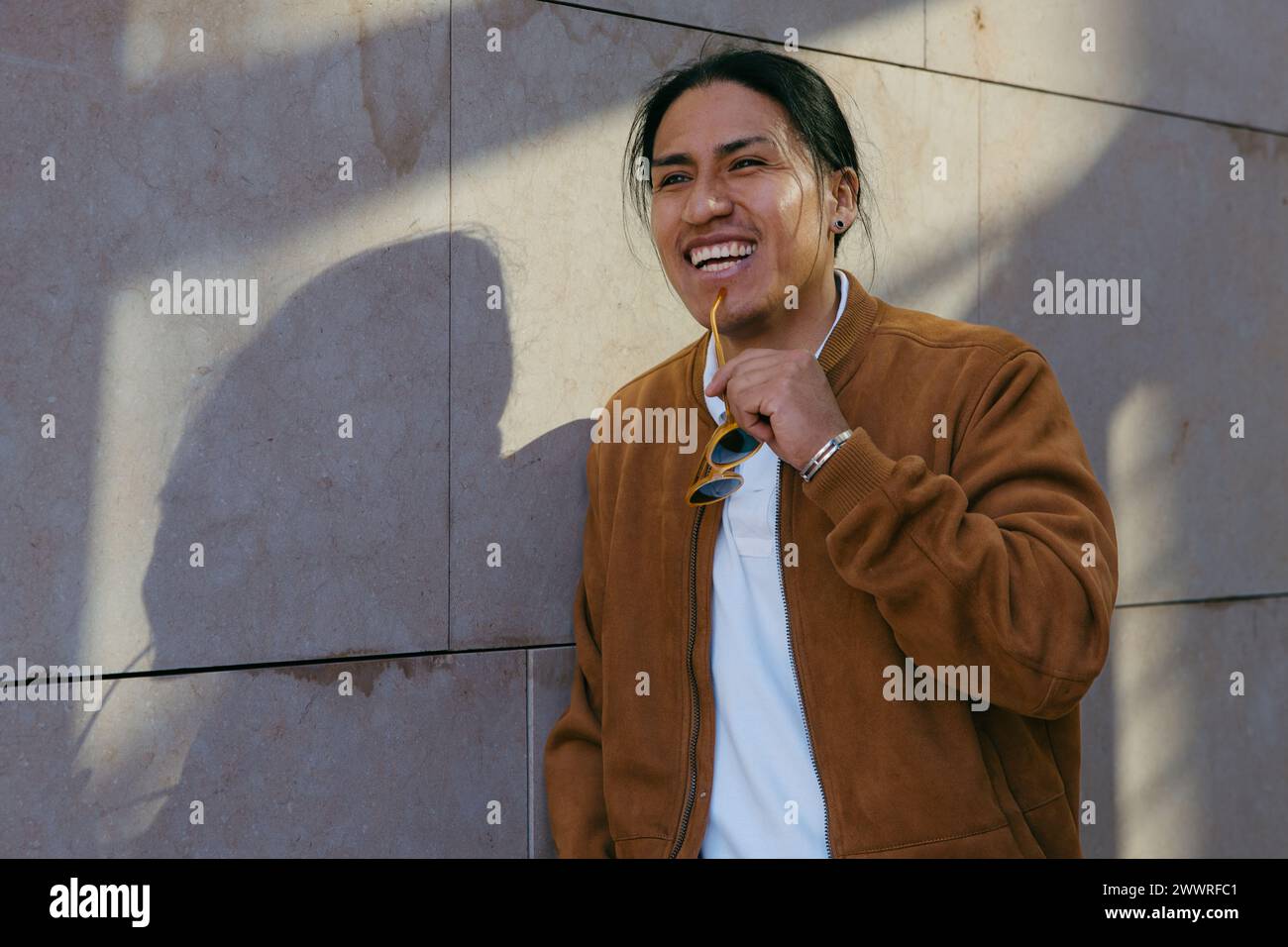 Un giovane vibrante sorpreso in un momento di risata, con gli occhiali da sole in una giornata di sole, che irradia positività Foto Stock