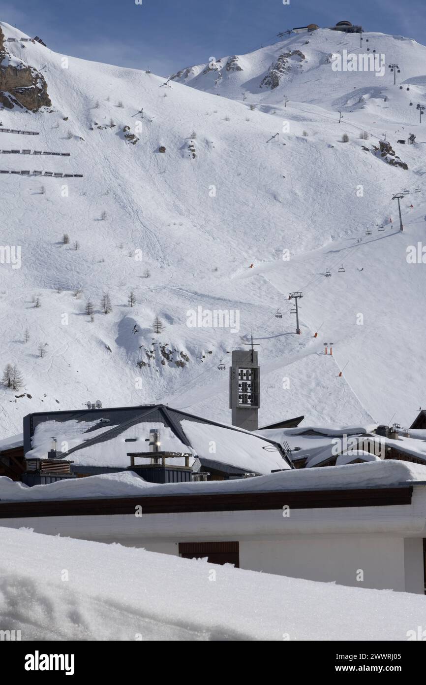 Il campanile della chiesa cattolica romana modernista sbircia sui tetti innevati di Tignes, una stazione sciistica costruita appositamente nelle Alpi francesi. Foto Stock