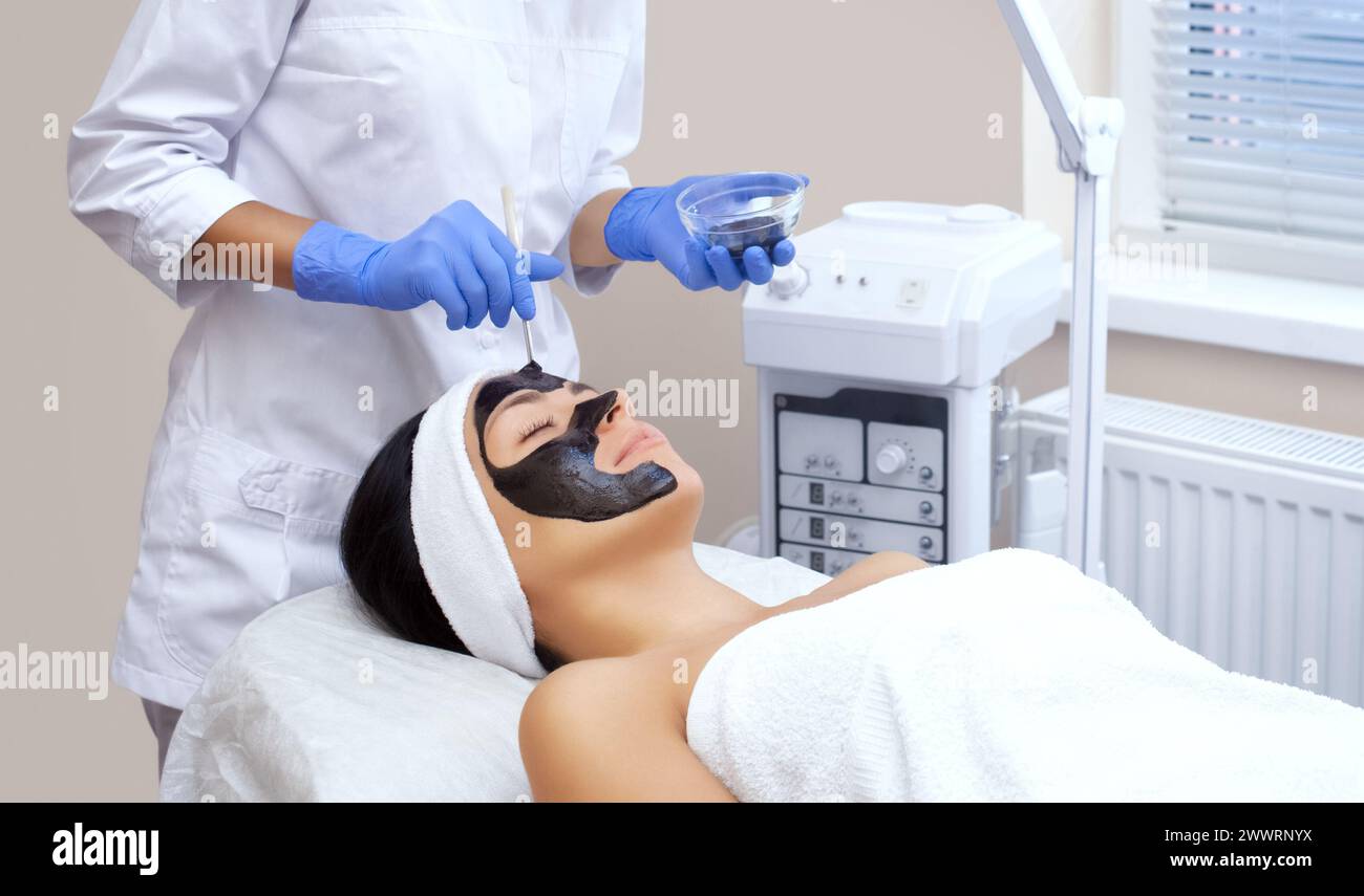 La procedura per applicare una maschera nera al volto di una bella donna. Trattamenti e cure termali nel salone di bellezza. Foto Stock