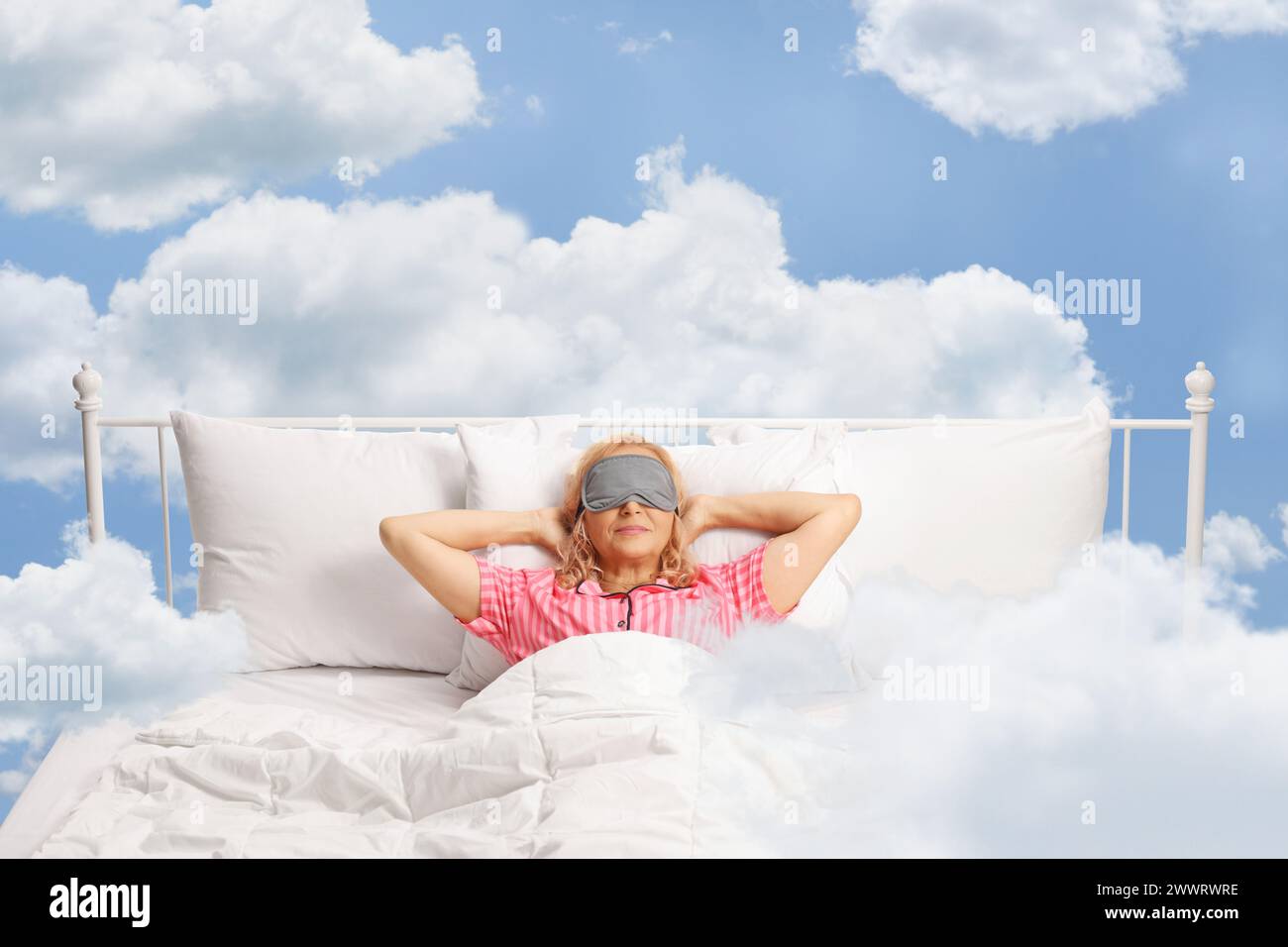 Donna tra le nuvole che riposa in un letto con la maschera sugli occhi Foto Stock