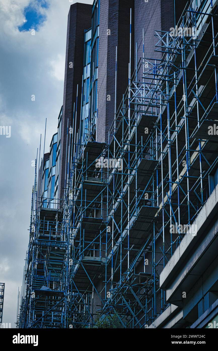 Cantiere urbano con intricate impalcature contro un edificio moderno sotto un cielo nuvoloso a Leeds, Regno Unito. Foto Stock