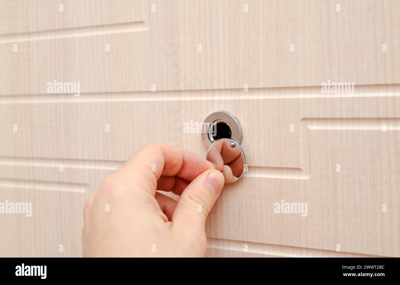 Mano vicino allo spioncino della porta su una nuova porta di legno. Foto di alta qualità Foto Stock