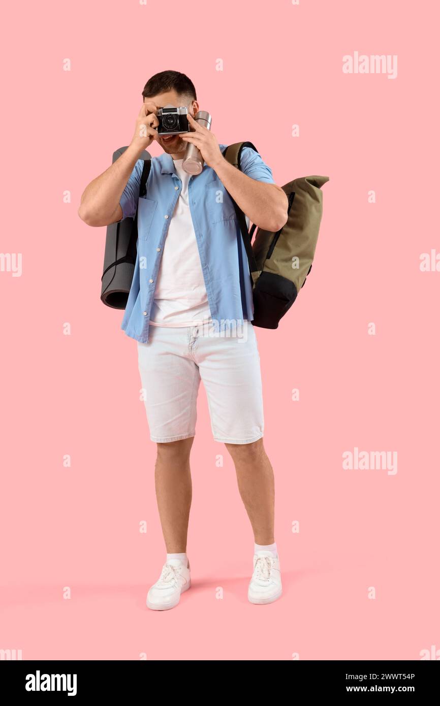Turista maschile con zaino e macchina fotografica che scatta foto di qualcosa su sfondo rosa Foto Stock
