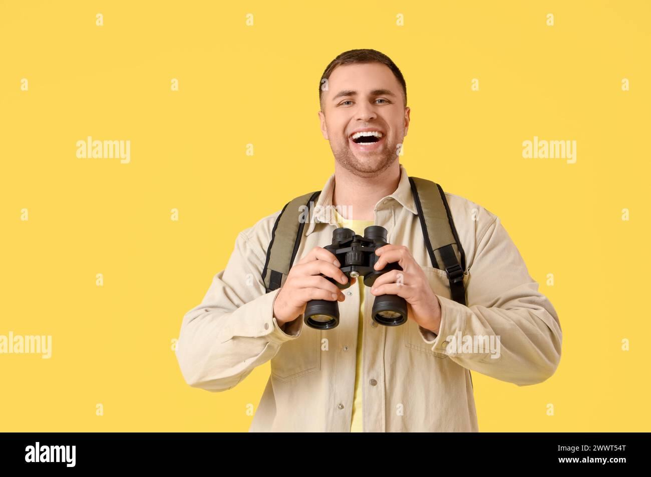 Turista maschile con zaino e binocolo su sfondo giallo Foto Stock