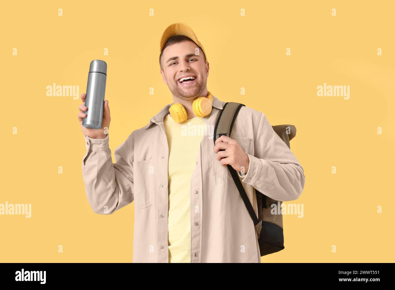 Turista maschile con zaino e thermos su sfondo giallo Foto Stock