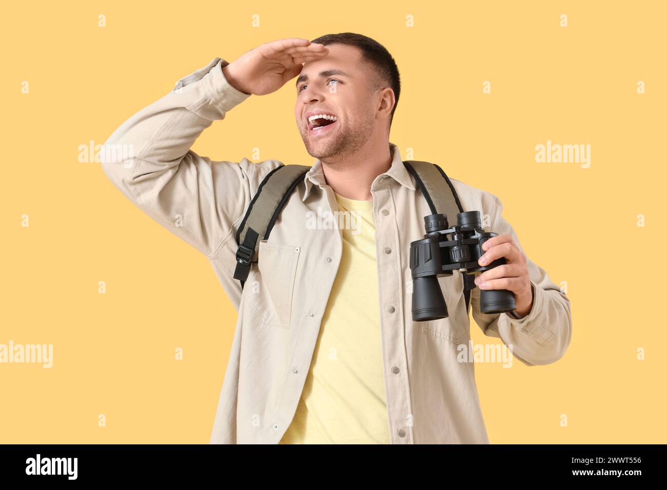 Turista maschile con zaino e binocolo su sfondo giallo Foto Stock