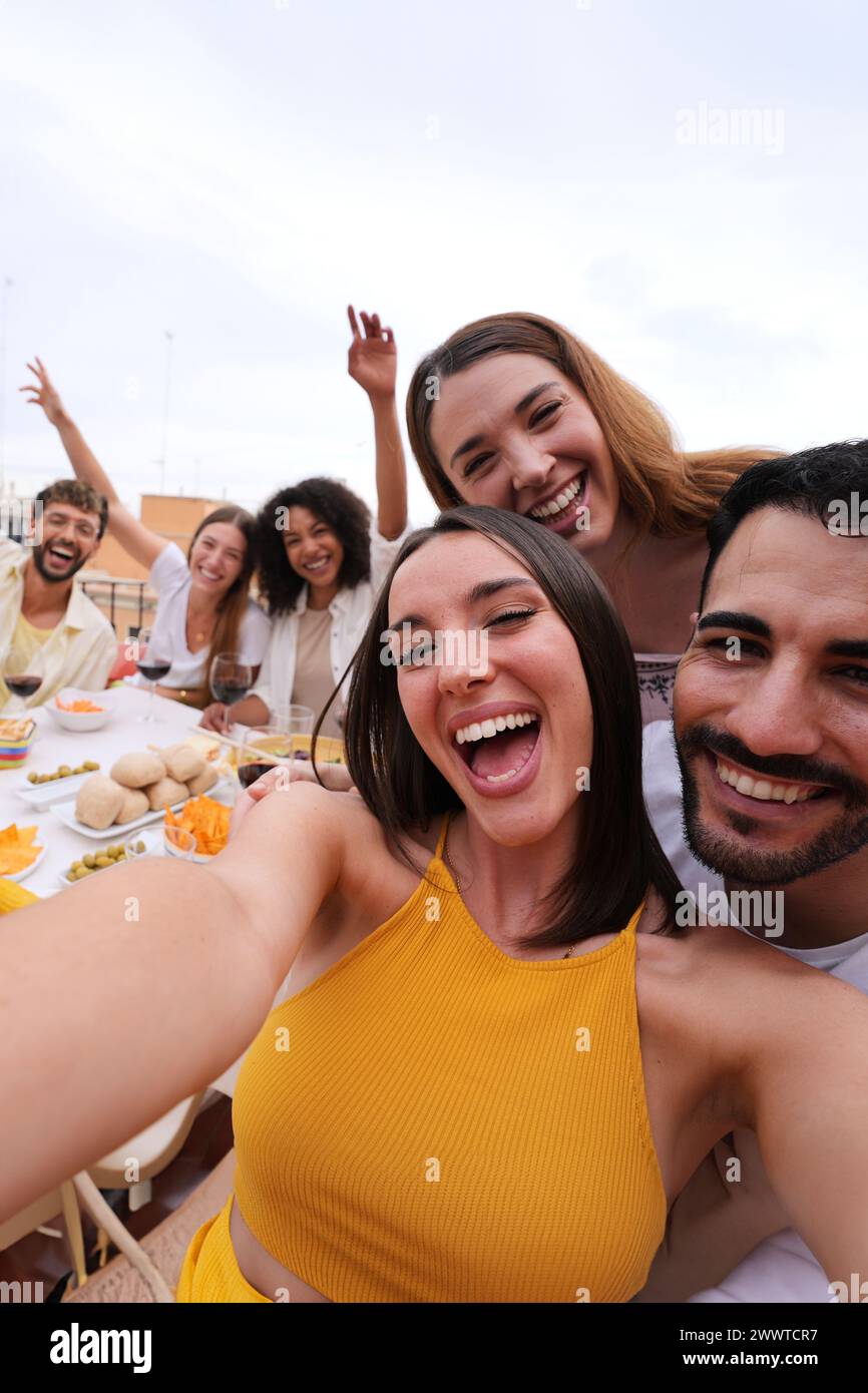 Eccitata giovane bella donna che scatta selfie di gruppo con amici gioiosi sul tetto. Foto di gente allegra Foto Stock