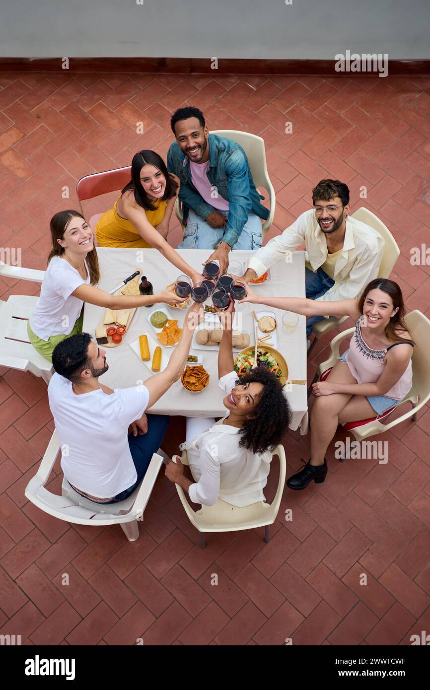 Ritratto dall'alto di giovani amici multirazziali che brindano bicchieri di vino rosso per festeggiare la festa sul tetto. Foto Stock