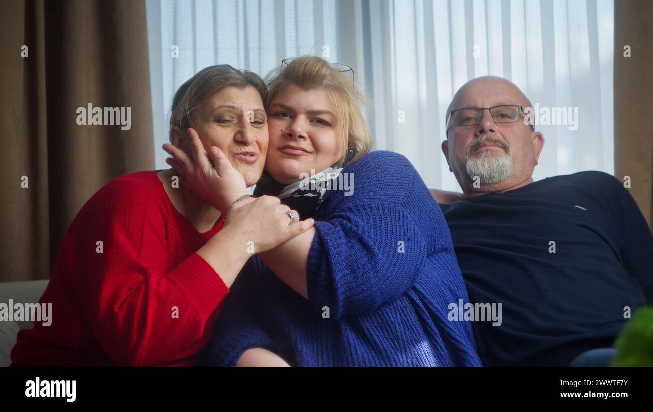 Famiglia felice seduta sul divano sorridente guardando la fotocamera, posare, divertirsi, fare gesti divertenti. Ritratto di famiglia felice Foto Stock